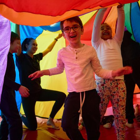 Groupe d'enfants jouant joyeusement sous un grand drap coloré lors d'un stage Toup’ti Gym, favorisant l'épanouissement et la socialisation