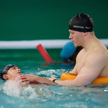 Un enfant accompagné par un moniteur de natation lors d'une session sécurisée au stage Toup’ti Gym, alliant plaisir et sécurité